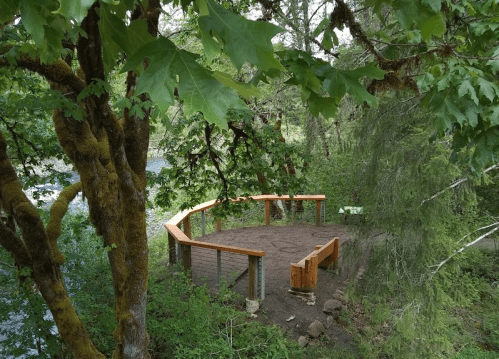 A wooden platform surrounded by trees near a river, with a natural, serene setting.