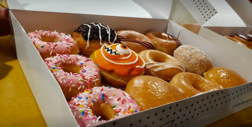 A box of assorted donuts, including pink frosted, chocolate-covered, and a Halloween-themed donut with orange icing.