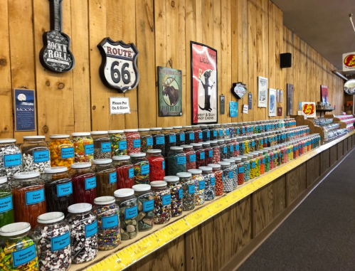 A colorful display of jars filled with various candies against a wooden wall, featuring Route 66 memorabilia.