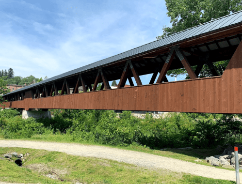 A wooden covered bridge spans a green landscape under a clear blue sky.