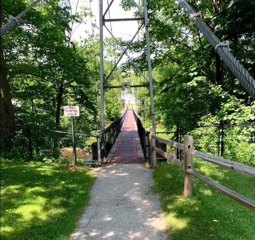 A pathway leads to a suspension bridge surrounded by greenery, with a sign indicating "No Trespassing."