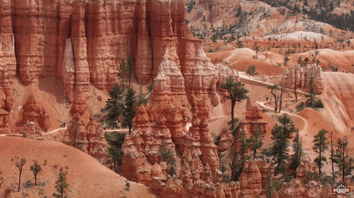 A scenic view of Bryce Canyon's red rock formations and trails, surrounded by green trees and a clear sky.