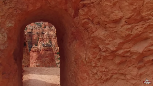 A natural rock arch frames a view of vibrant red rock formations in a desert landscape.