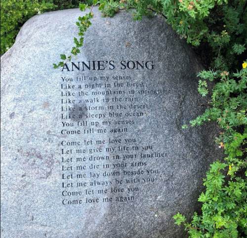 A stone engraved with the text of "Annie's Song," surrounded by greenery.