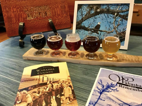 A wooden flight of craft beers, brochures about Wabasha County, and a framed photo of a bird on a branch.