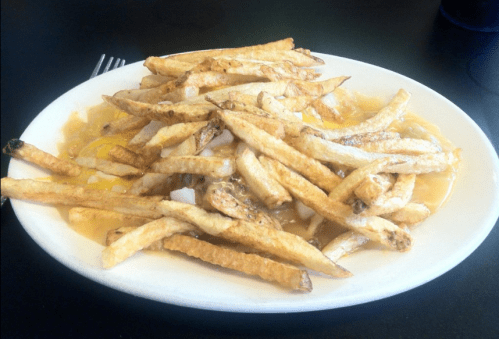 A plate of golden, crispy French fries topped with melted cheese and various toppings, served on a white dish.