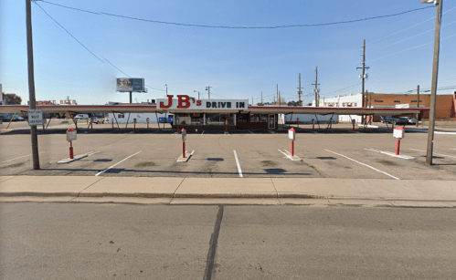 A retro drive-in restaurant with a long awning and empty parking lot, set against a clear blue sky.