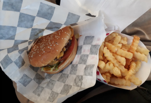 A sesame seed bun burger with lettuce, tomato, and cheese next to a container of crinkle-cut fries.