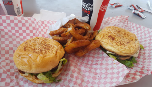 Two sesame seed burgers with lettuce, accompanied by a side of onion rings and a Coca-Cola drink.