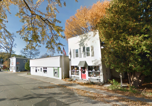 A quaint street scene featuring two buildings, one with a pink door, surrounded by autumn foliage.