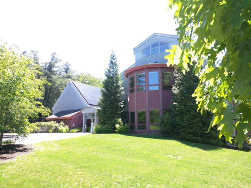 A modern house with large windows, surrounded by trees and a green lawn on a sunny day.