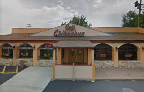 Exterior of Café Chihuahua, featuring a welcoming entrance, open sign, and decorative planters under a cloudy sky.