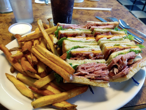 A hearty sandwich stacked with meats and cheese, served with a side of golden French fries and a drink.