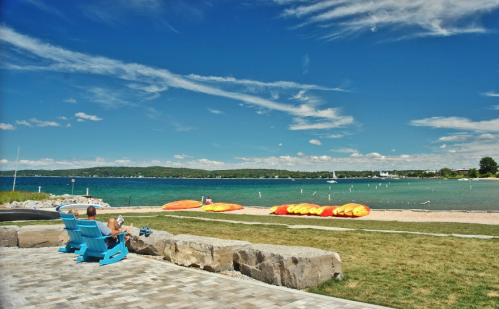 A serene beach scene with colorful kayaks on the shore, blue water, and a person relaxing in a chair.