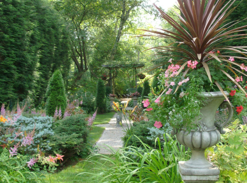 A lush garden path lined with colorful flowers and greenery, featuring a decorative planter in the foreground.