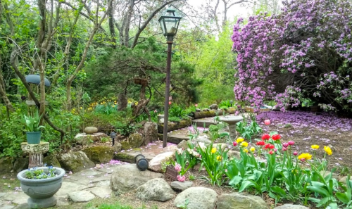 A vibrant garden path lined with flowers, a lamp post, and blooming trees, creating a serene outdoor scene.