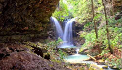 A serene waterfall cascades into a tranquil pool, surrounded by lush greenery and rocky cliffs.