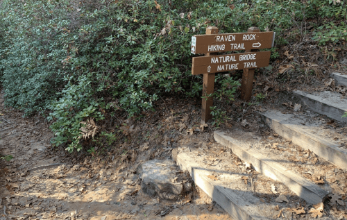 A wooden signpost at a trailhead indicates directions for Raven Rock Hiking Trail and Natural Bridge Nature Trail.