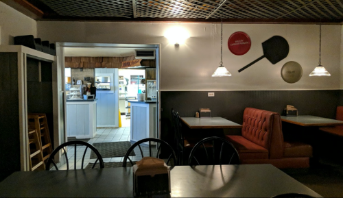 A dimly lit restaurant interior with empty tables, a red booth, and a doorway leading to the kitchen area.