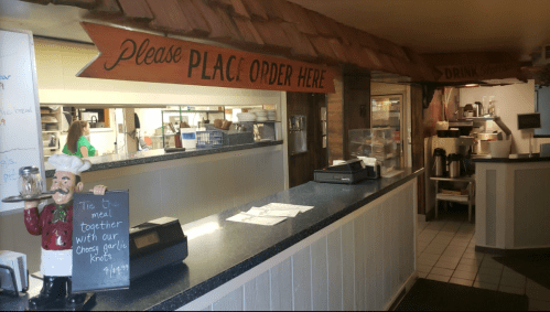 Interior of a restaurant with a counter, sign saying "Please Place Order Here," and a chef statue holding a menu board.