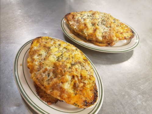 Two baked dishes topped with melted cheese and herbs, served on oval plates.
