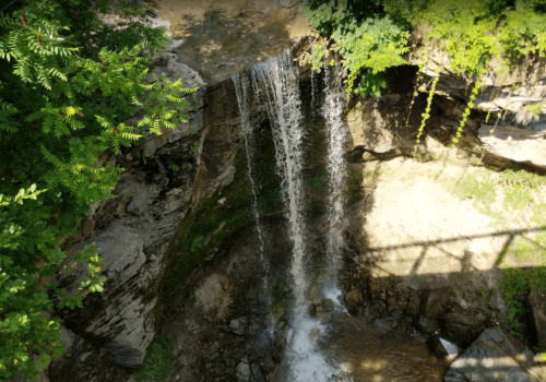 A serene waterfall cascading over rocks, surrounded by lush greenery and sunlight filtering through the leaves.