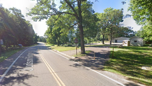A quiet road lined with trees, leading to a small parking area and a building in the distance on a sunny day.