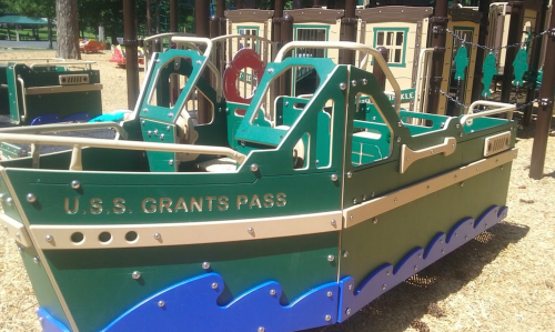 A colorful playground boat structure named "U.S.S. Grants Pass" on a sandy surface.