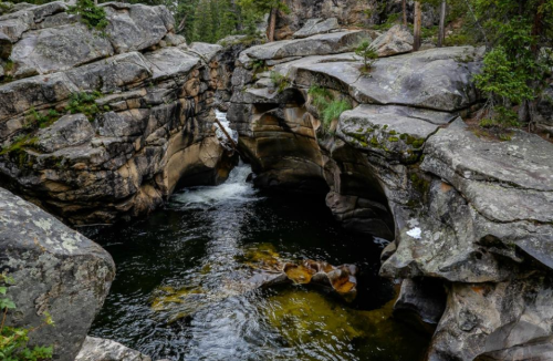 A serene river flows through a rocky canyon, surrounded by lush greenery and towering trees.