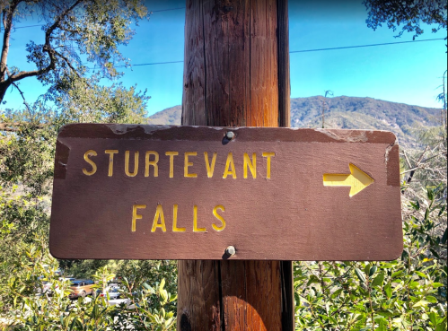Wooden sign pointing right to Sturtevant Falls, surrounded by trees and mountains in the background.