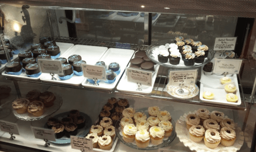 A display case filled with various decorated cupcakes and desserts, featuring colorful frosting and decorative toppings.