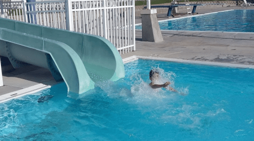 A child splashes into a pool after sliding down a water slide on a sunny day.