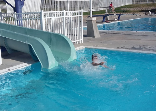 A child splashes into a pool after sliding down a water slide on a sunny day.