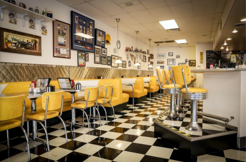A retro diner interior with yellow booths, checkered floor, and vintage decor on the walls.