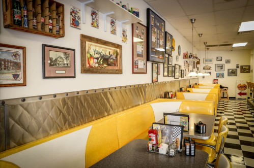 A retro diner interior with yellow booths, checkered floor, and vintage decor on the walls.