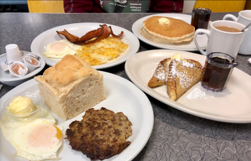A breakfast spread featuring eggs, bacon, pancakes, hash browns, French toast, and coffee on a table.
