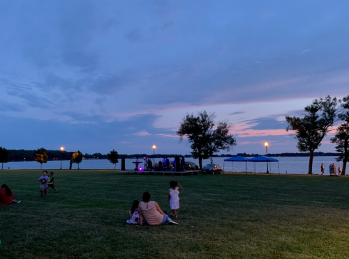 A serene lakeside park at dusk, with families enjoying the evening and colorful lights in the background.