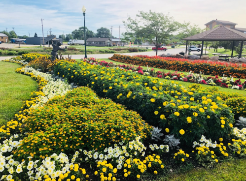 A vibrant flower garden featuring yellow, white, and red blooms, with a gazebo and a statue in the background.