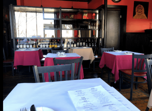 Interior of a restaurant featuring red walls, tables with pink tablecloths, and a display of bottles in the background.