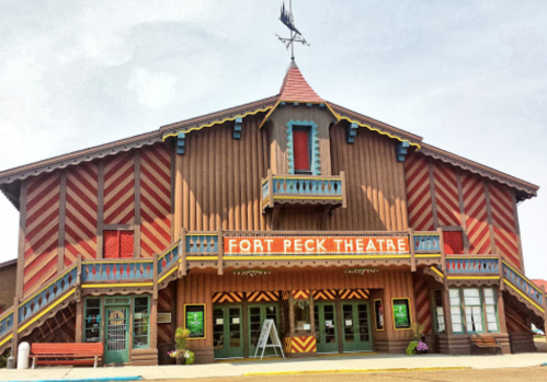 Colorful wooden facade of Fort Peck Theatre with decorative patterns and a peaked roof under a clear sky.