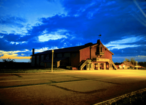 A historic building illuminated at dusk, with dramatic clouds and a colorful sky in the background.