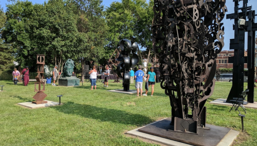 A group of people exploring an outdoor sculpture park with various large metal sculptures and greenery.