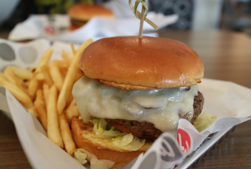 A close-up of a cheeseburger with melted cheese, lettuce, and a side of golden fries on a paper tray.