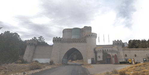 A large, castle-like building with turrets and an arched entrance, set against a cloudy sky and surrounded by trees.