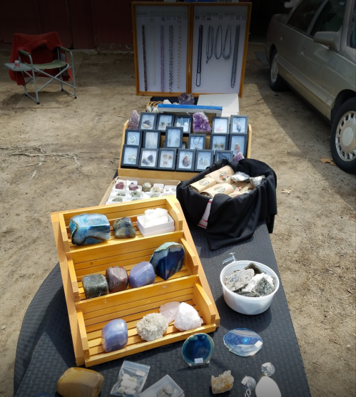 A display of various gemstones and crystals on a table, with additional jewelry and items in the background.