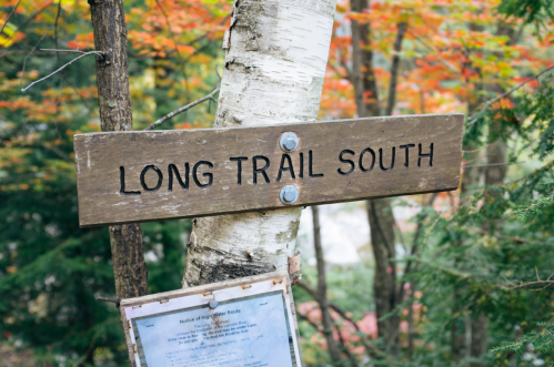 Wooden sign reading "LONG TRAIL SOUTH" attached to a tree, surrounded by colorful autumn foliage.