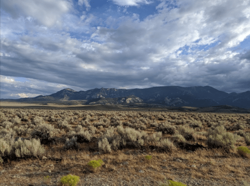 A vast landscape featuring sagebrush and mountains under a cloudy sky.