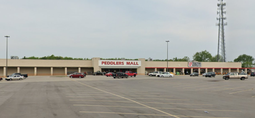 Exterior view of Peddlers Mall with a large parking lot and a cell tower in the background.