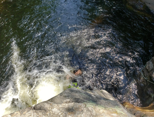 A person swimming in a dark, swirling pool of water near a rocky edge, with sunlight reflecting on the surface.
