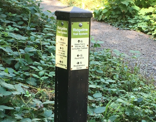 Trail signpost for Ridgeline Trail System, indicating nearby trails and directions in a lush, green environment.